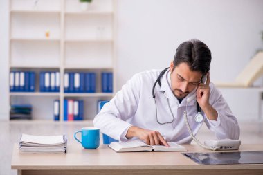 Klinikte kitap okuyan genç bir erkek doktor.