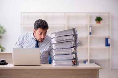 Genç bir erkek çalışan ve ofiste çok fazla iş var.