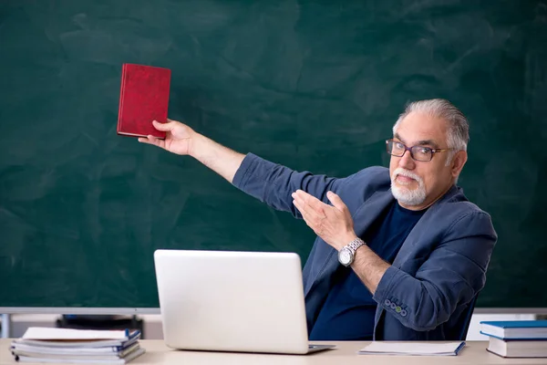 Старый учитель мужского пола держит книгу в классе — стоковое фото