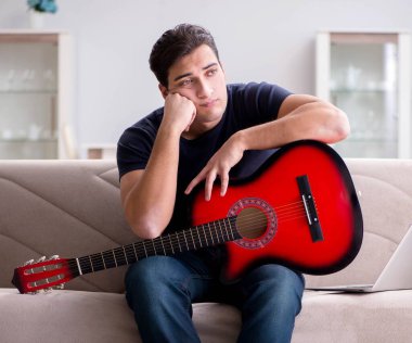 Genç adam evde gitar çalıyor.