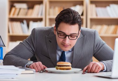 Aç komik iş adamı abur cubur sandviç yiyor.