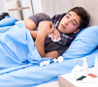 Grip olmuş hasta adam yatakta yatıyor.