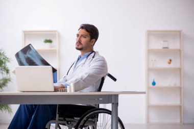 Klinikte çalışan tekerlekli sandalyedeki genç erkek doktor.