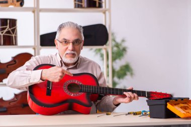 Yaşlı erkek tamirci iş yerinde müzik aletlerini tamir ediyor.