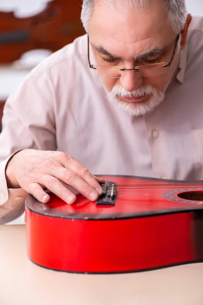 Alte männliche Reparaturkraft repariert Musikinstrumente am Arbeitsplatz — Stockfoto