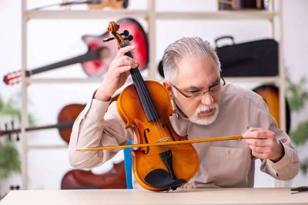 Oude mannelijke reparateur repareert muziekinstrumenten op het werk — Stockfoto