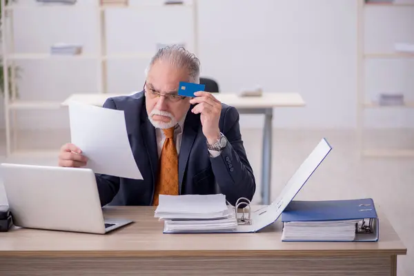 Homem velho empregado segurando cartão de crédito no escritório — Fotografia de Stock