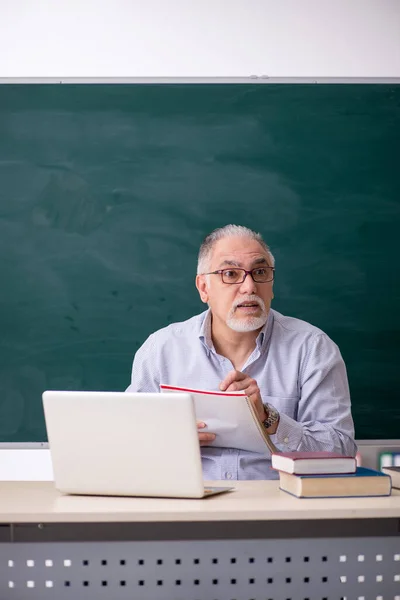 녹색 칠판 앞에 앉아 있는 늙은 남성 교사 — 스톡 사진