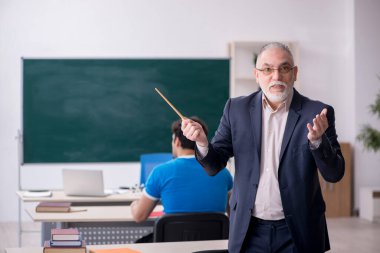 Yaşlı erkek öğretmen ve genç erkek öğrenci tahtanın önünde.