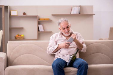 Yaşlı adam evde alkol içiyor.