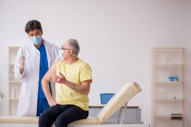 Yaşlı erkek hasta aşılama bölümünde genç bir erkek doktor.