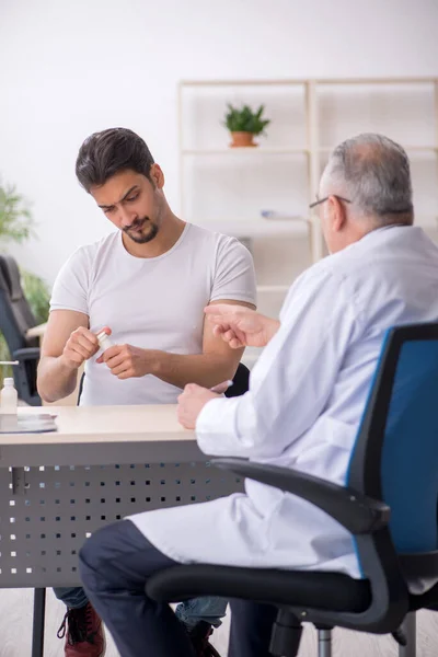 Old male doctor suggesting pills to young male patient — Stock Photo, Image
