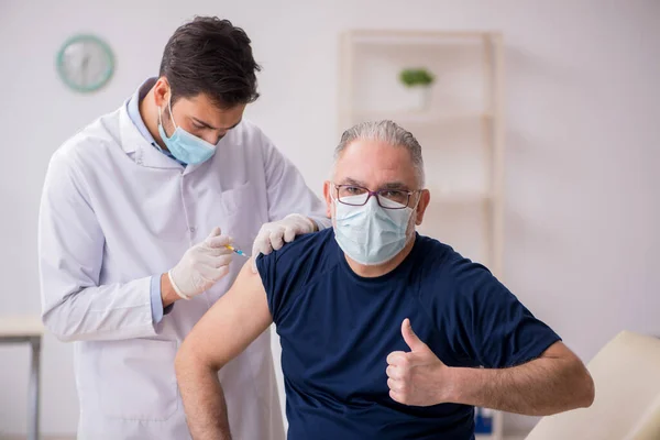 Старий пацієнт, який відвідує молодого лікаря під час вакцинації — стокове фото