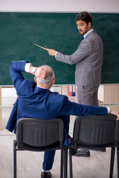 Young male employee and old boss in front of blackboard — Stock Photo, Image