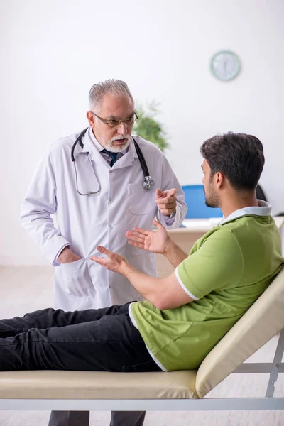 Joven hombre visitando viejo médico masculino — Foto de Stock