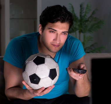 Genç adam gece geç saatlerde futbol seyrediyor.