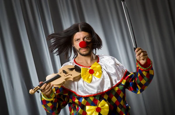 Смешной клоун прилипает скрипку к занавеске — стоковое фото