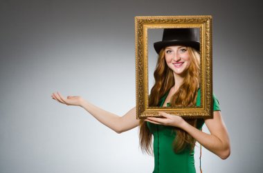 Elinde resim çerçevesi olan yeşil elbiseli bir kadın.