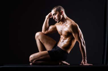 Kaslı adam karanlık stüdyoda poz veriyor.