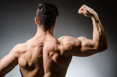 Kaslı adam karanlık stüdyoda poz veriyor.