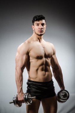 Vücut geliştirmeci dumbbells ile gri arka plan üzerinde yırtık kas