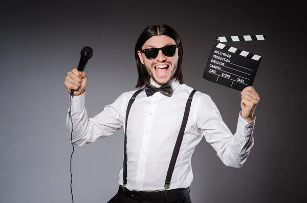 Hombre positivo sosteniendo clapperboard y micrófono aislado en gris — Foto de Stock