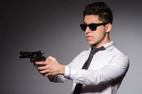 Hombre joven en gafas de sol fresco sosteniendo arma aislada en gris — Foto de Stock