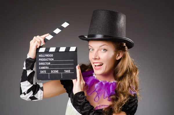 Hezká dívka v kostýmu šaška drží klapku proti šedi — Stock fotografie