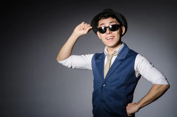 Hombre joven en gafas de sol en chaleco azul y sombrero contra gris — Foto de Stock