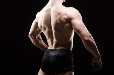 Kaslı adam karanlık stüdyoda poz veriyor.