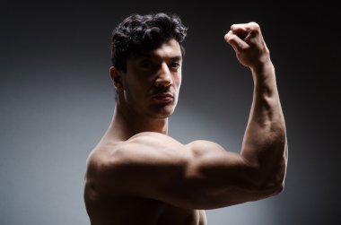 Kaslı adam karanlık stüdyoda poz veriyor.