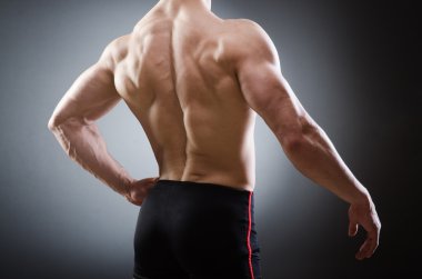 Kaslı adam karanlık stüdyoda poz veriyor.