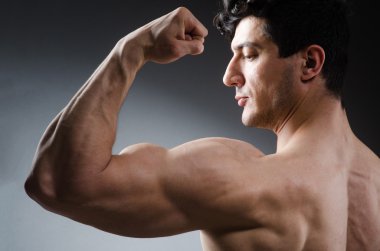 Kaslı adam karanlık stüdyoda poz veriyor.