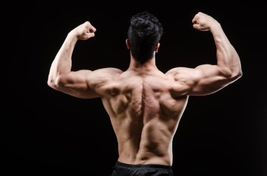 Kaslı adam karanlık stüdyoda poz veriyor.