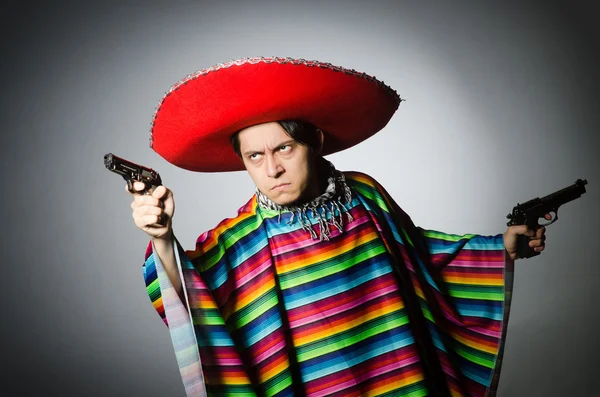 Человек в ярком мексиканском пончо держит пистолет против серого — стоковое фото