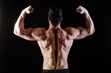 Kaslı adam karanlık stüdyoda poz veriyor.