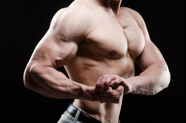 Kaslı adam karanlık stüdyoda poz veriyor.