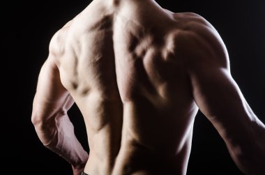 Kaslı adam karanlık stüdyoda poz veriyor.