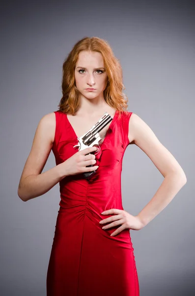Ragazza in abito rosso con pistola contro grigio — Foto Stock