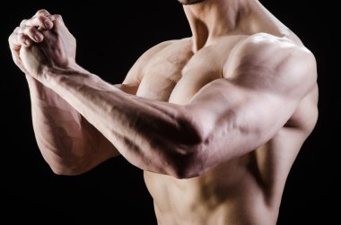 Kaslı adam karanlık stüdyoda poz veriyor.