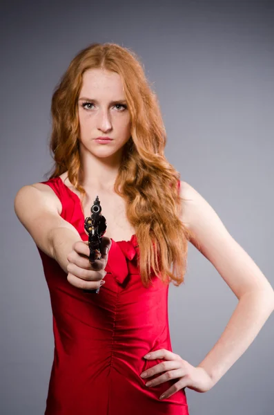 Chica en vestido rojo con pistola contra gris — Foto de Stock