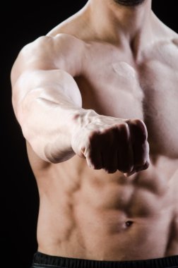 Kaslı adam karanlık stüdyoda poz veriyor.