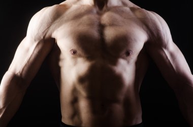 Kaslı adam karanlık stüdyoda poz veriyor.