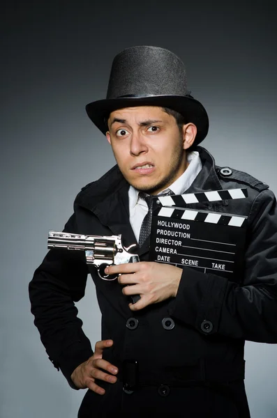 Joven con arma y tabla de aplausos contra gris — Foto de Stock