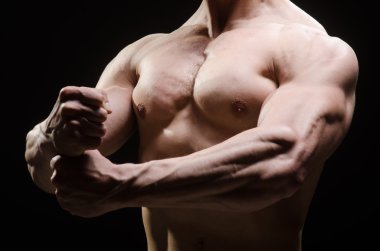 Kaslı adam karanlık stüdyoda poz veriyor.