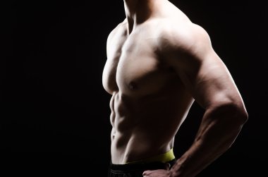 Kaslı adam karanlık stüdyoda poz veriyor.