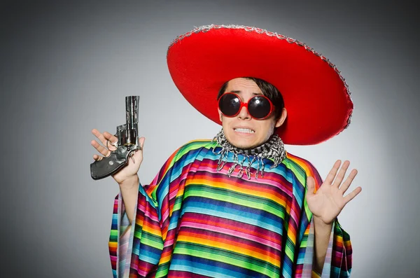Muž v živém mexickém pončo drží ruční zbraň proti šedé — Stock fotografie