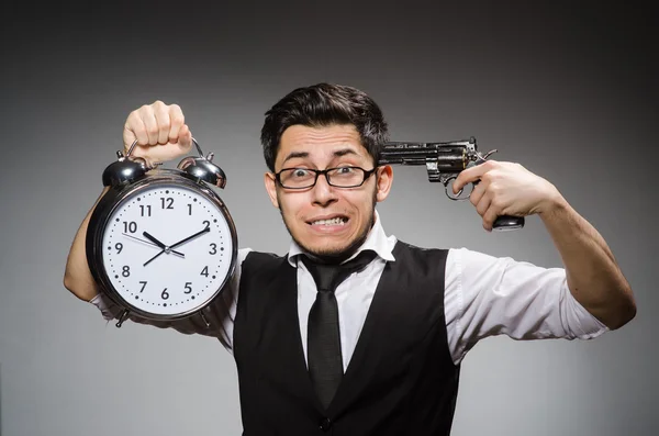 Employee holding alarm clock and handgun against gray — Stock Photo, Image