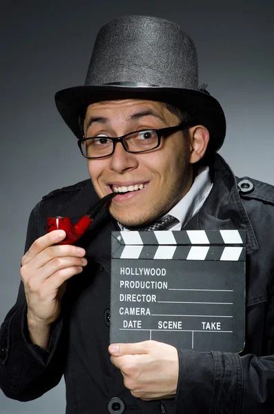 Detective in black coat with clapperboard against gray — Stock Photo, Image