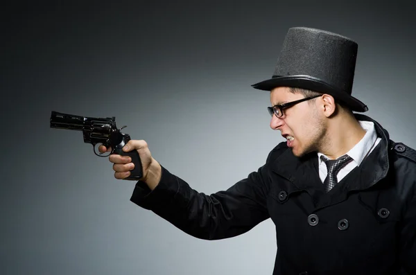 Zločinec v černém kabátě, drží hadgun proti šedi — Stock fotografie